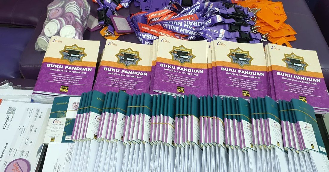 Tumpukan buku panduan umroh ungu dan lanyard ID card yang sudah disiapkan sebelum keberangkatan
