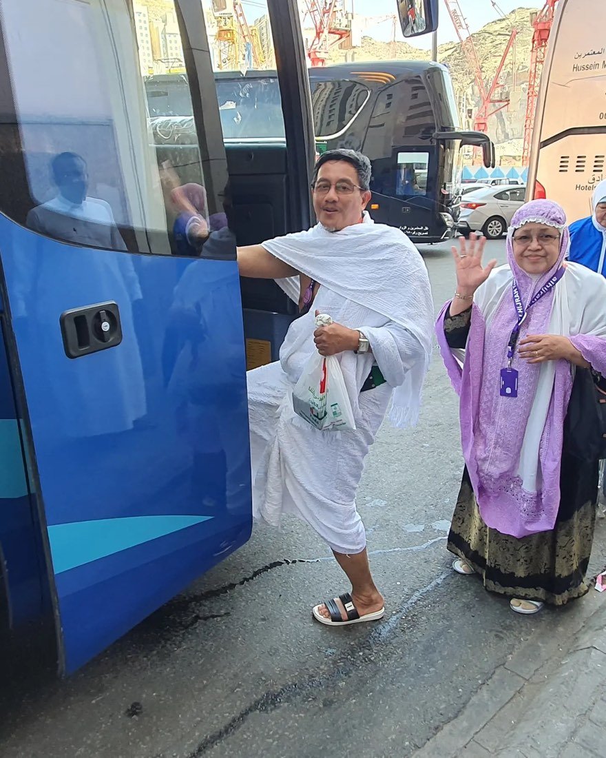 Sepasang jamaah berihram melambaikan tangan saat menaiki bus