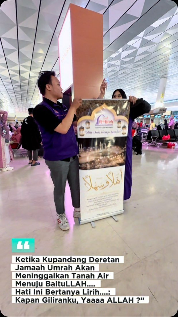 Petugas Al Hijrah berseragam ungu di samping standee sambutan jamaah di area keberangkatan bandara